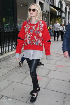 a woman walking down the street in black leather pants and a red sweater with flowers on it