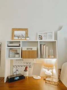 a wooden desk topped with a lamp next to a white book shelf filled with books