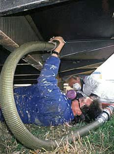 two men working under a truck with hoses attached to the side of it and one man wearing a gas mask on his head