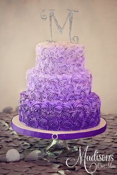 a three tiered cake with purple icing and the letter m on top