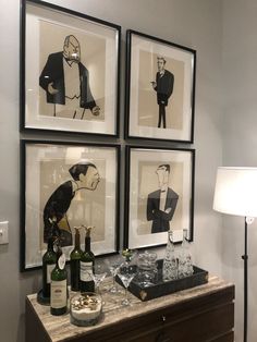 three framed pictures on the wall above a dresser with bottles and glasses in front of it