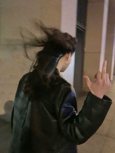 a woman with her hair blowing in the wind while standing on a sidewalk next to a building