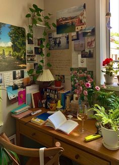 a wooden desk topped with lots of books next to a window covered in pictures and plants