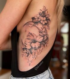 a woman's back tattoo with flowers and leaves on her left side ribcage