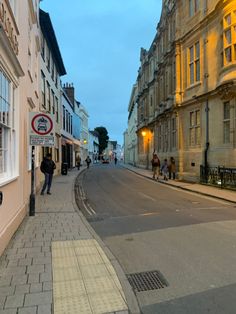 people are walking down the street in front of some buildings at dusk, and one person is on his cell phone