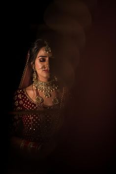 a woman in a red and gold bridal outfit looking at the camera with her eyes closed