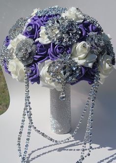 the bridal bouquet is adorned with purple and white roses, silver beads, and crystal jewels