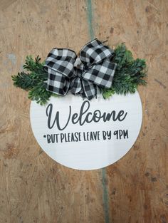 a welcome sign hanging from the side of a wooden door with a bow on it