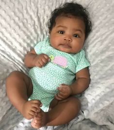 a baby is sitting on a bed and smiling at the camera while wearing a green onesie