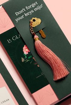 a brochure with a tassel and keychain attached to it on a pink background