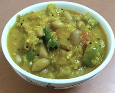 a white bowl filled with beans and vegetables on top of a wooden table next to a spoon