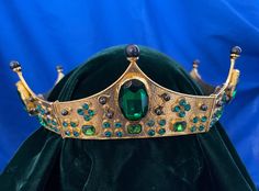 a crown with green stones and jewels on it's headdress is shown in front of a blue background