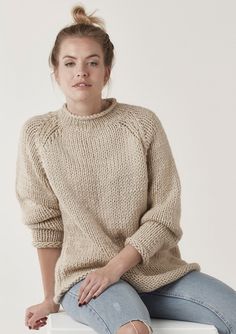 a woman sitting on top of a white box wearing ripped jeans and a beige sweater