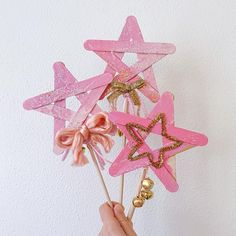 a hand holding three pink star picks with gold glitters on them and a bell in the middle