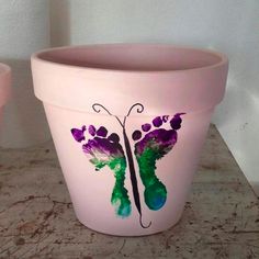 a pink flower pot with purple flowers painted on the side and green butterflies drawn on it