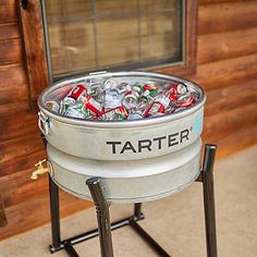 a cooler filled with soda cans sitting in front of a wooden wall and floor next to a window