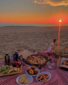 a picnic on the beach at sunset with pizza, fruit and beer in front of it