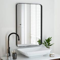 a white sink sitting under a large mirror next to a potted plant on a counter