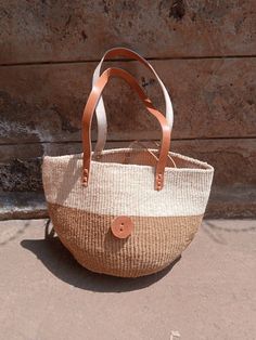 "Natural sisal kiondo bag with stitched leather straps. Ideal for the beach 🏖️, with a casual wear and a perfect accessory for an evening out with friends. This unique tote bag is handmade by a group of ladies in a remote rural village in Machakos, Kenya. DIMENSIONS Bottom width: 10\"/25.5cm Top width: 14\"/35.56cm Depth: 10\"/25.5cm Straps: 15\"/38cm SHIPPING All orders ship via DHL Express (3-5) days delivery time." Basket Toy Storage, African Home, Unique Tote Bag, Toy Storage Baskets, Fall Bags, African Home Decor, Market Basket, Basket Woven, Home Decor Baskets