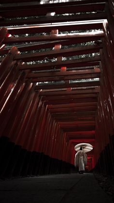 a man walking down a long hallway with red lights on it's ceiling and an umbrella over his head