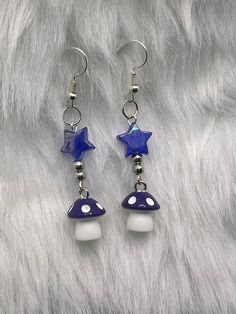 Each earring measures approximately 2 1/4" in length. Step into a world of enchantment with our Purple Mushroom Dangle Handmade Earrings. These whimsical earrings feature charming purple mushroom charms and iridescent star beads. Each mushroom charm is suspended from elegant, hypoallergenic hooks, ensuring both comfort and style for everyday wear. The rich purple hue of the mushrooms adds a pop of color and a touch of magic to any ensemble, making these earrings a standout accessory. The intrica Diy Dangling Earrings, Purple Jewelry Aesthetic, Beaded Star Earrings, Handmade Dangle Earrings In Fairycore Style, Handmade Fairycore Dangle Earrings, Handmade Cute Mushroom Earrings, Glass Mushroom Earrings, Earrings Mushroom, Diy Earrings Dangle