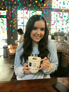 a woman sitting at a table holding a coffee cup with confetti on it