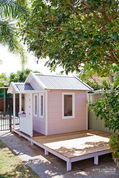 a small pink house sitting on top of a wooden platform next to a fence and trees