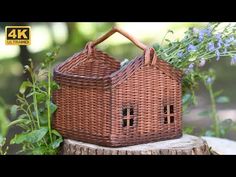 a wicker house sitting on top of a tree stump next to purple flowers and greenery