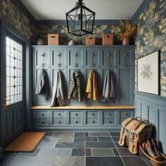 an entryway with blue cabinets and wallpaper, hanging coats on the door hooks