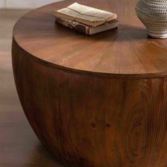 a round wooden table with a vase and book on it's top, in front of a white wall