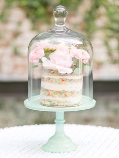 a cake under a glass dome with pink flowers on top and sprinkles