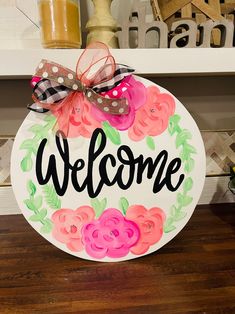 a welcome sign with flowers painted on it and a bow hanging from the front door