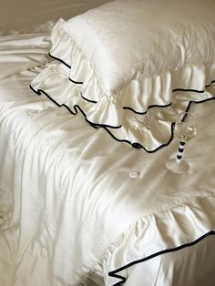 an unmade bed with white sheets and black piping on the pillowcases