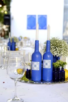 two blue wine bottles sitting on top of a table next to some glasses and flowers