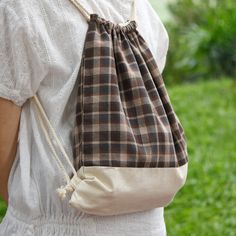 a woman carrying a brown and white bag on her back while standing in the grass