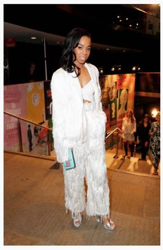 a woman standing in front of a crowd wearing white clothing and holding a blue purse