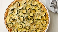 a pie with zucchini and cheese on it next to a fork and knife