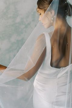 a woman wearing a white wedding dress and holding a veil over her head with one hand