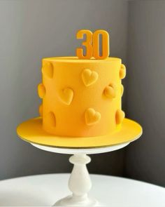 a yellow cake with hearts and the number 30 on top is sitting on a white pedestal