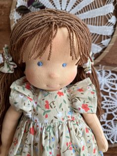 a doll with brown hair and blue eyes wearing a dress in front of a doily