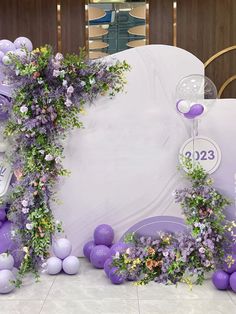 purple flowers and balloons are on display in front of a white backdrop