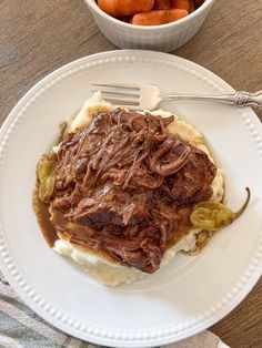 a white plate topped with meat and mashed potatoes next to a bowl of carrots