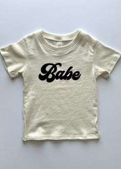 A must-have for your precious babe! Product Details: Color: Ivory/Off White Tees are a natural color made of organic cotton. Perfect for all the babes out there. "Babe" is fuzzy, black flock for a vintage feel. 100% Combed Ring Spun Organic Cotton Unisex tee Machine wash cold Handmade in USA 100% Organic Cotton Cute Unisex Organic Cotton Tops, Cute Soft-washed Organic Cotton Tops, Off White Tees, Color Ivory, Tee Shop, Natural Color, Baby Onesies, Baby Clothes, Organic Cotton