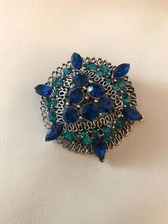 "Vintage Silver Tone With Blue And Green Rhinestone Brooch/ Pin. The rhinestones are dark blue and teal green on the brooch. All rhinestones are prong set. The silver tone metal has open design work. There are 6 blue stones in the center and 6 blue marquis shaped rhinestones around the edge. Round teal stones fill in the rest of the brooch. The back of the brooch has a rollover safety clasp that works great. The brooch measures approx. 1.50\" diameter. All the rhinestones are attached and brooch Raggedy Ann Doll, Blue Stones, Vintage Monet, Vintage Spring, Pin Pendant, Open Design, Rhinestone Brooches, Metal Style, Teal Green