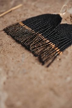 a close up of a black and gold beaded object on the ground next to a pair of knitting needles