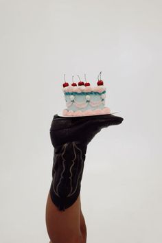 a hand holding up a cake with cherries on it in front of a white background