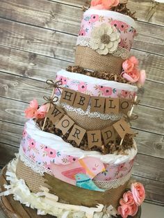 a three tiered cake with flowers and burlocks on the top is decorated with words that read hello world