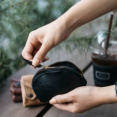 a person is holding a small black purse on a wooden table next to a coffee cup