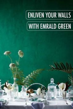 a table topped with lots of vases filled with flowers next to a green wall