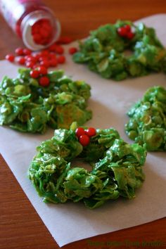 green cookies with red berries and sprinkles sitting on top of a piece of paper